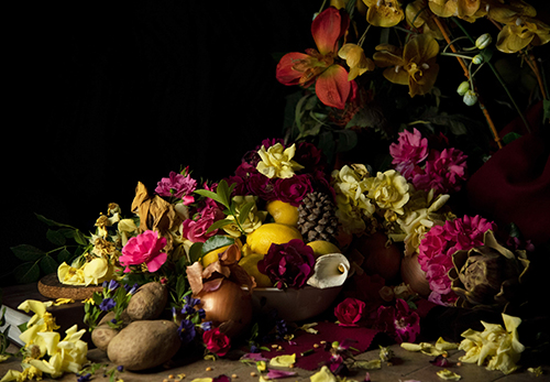 Photo of flowers and fruit bowl on table with dark background.